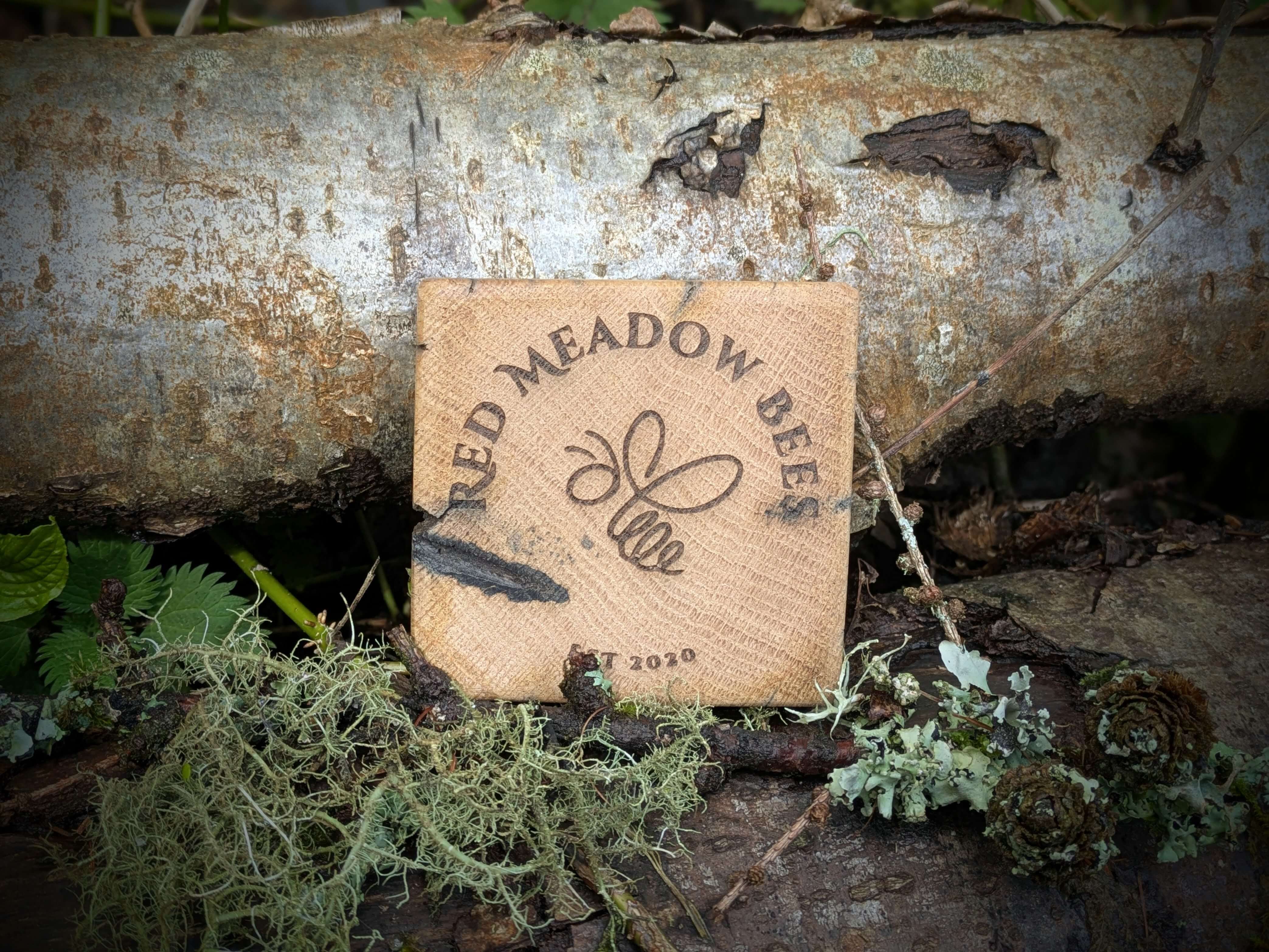 Wooden sign with 'Red Meadow Bees' logo on a natural background