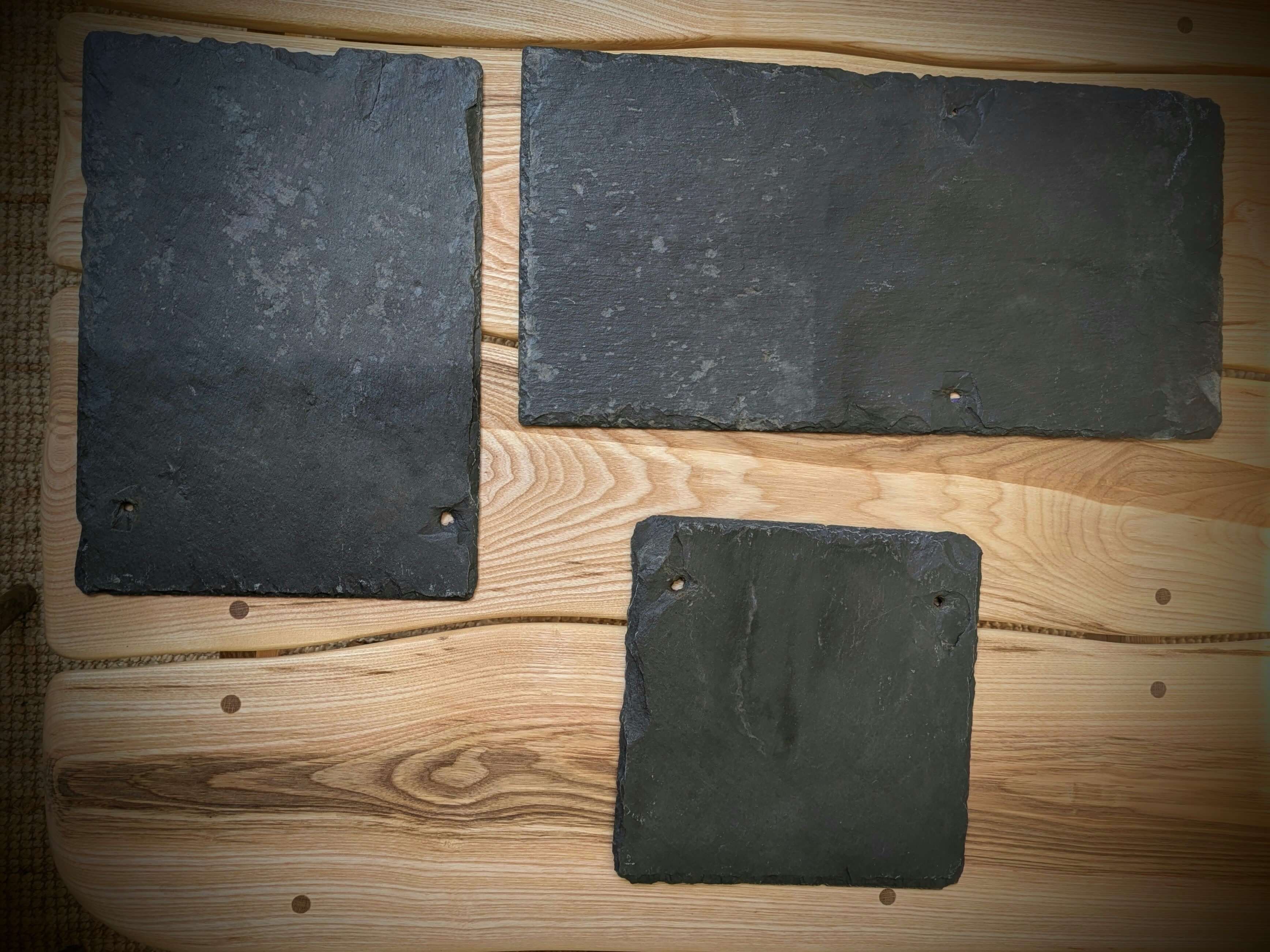 Three square slate tiles on a wooden surface