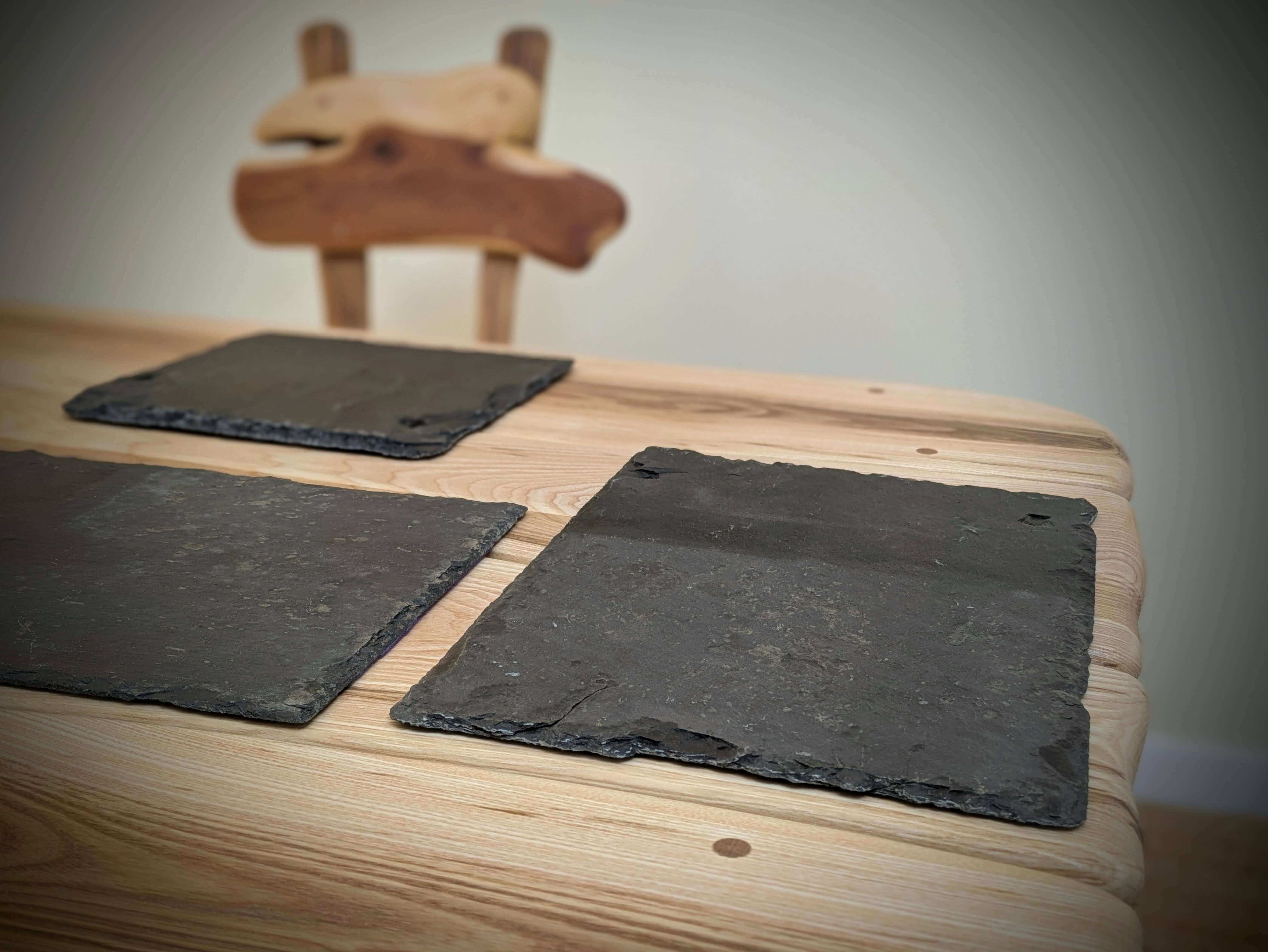 Slate coasters on a wooden table with a blurred chair in the background